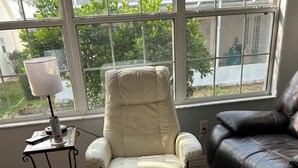 Ein Zimmer mit einem beigen Liegestuhl, einer schwarzen Ledercouch und einem kleinen Tisch mit einer Lampe.