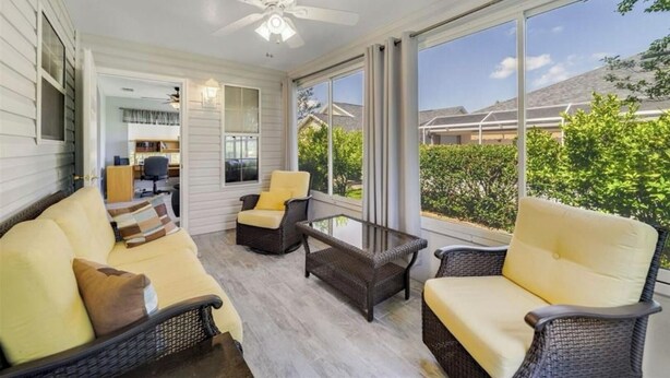 Eine überdachte Veranda mit Korbmöbeln, einem Deckenventilator und großen Fenstern mit Blick auf die Nachbarschaft.