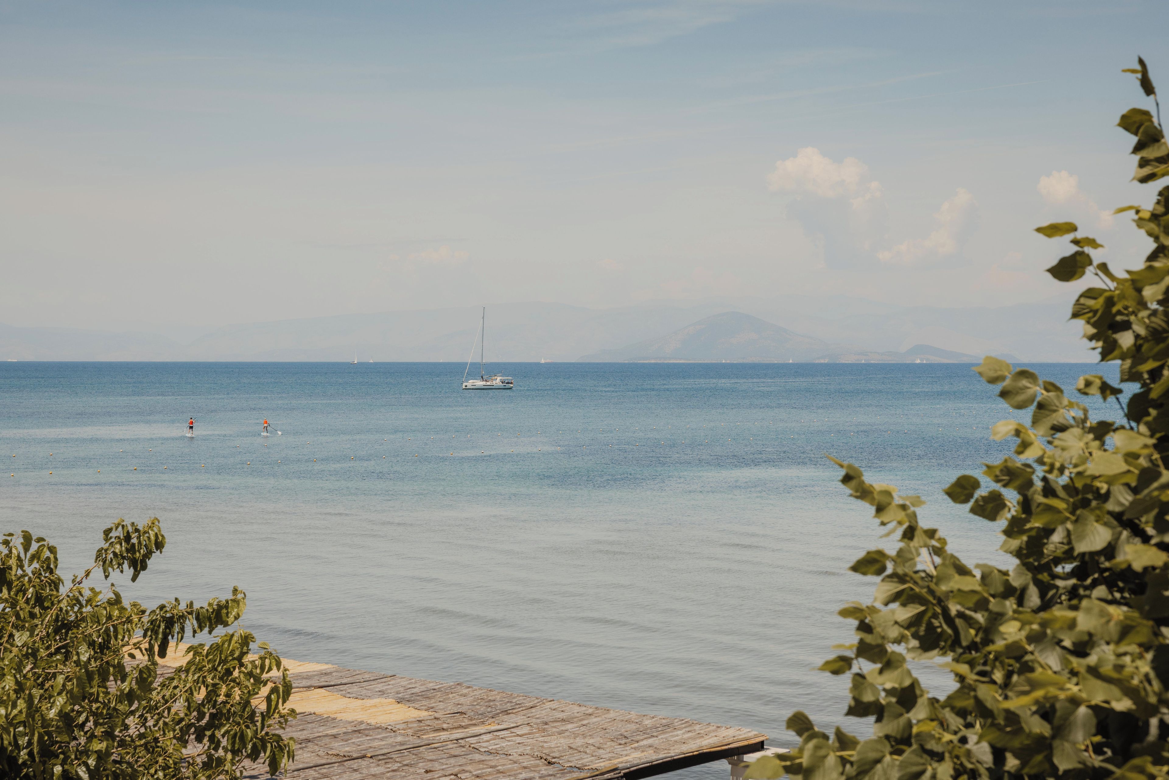A calm sea with a wooden dock and distant mountains.