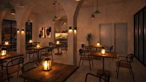 An indoor dining area with wooden tables and chairs, hanging pendant lights, and a view of the outside. - Cavo Notos Beach Hotel (Lefkimmi)