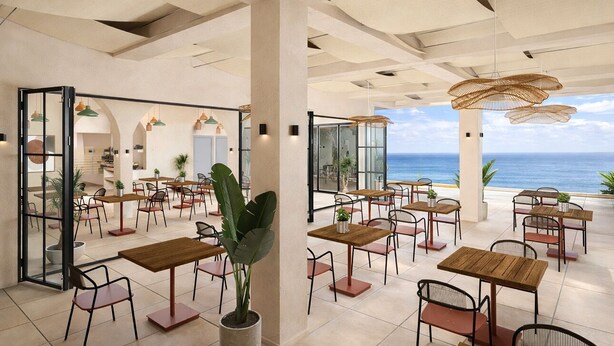 A spacious outdoor dining area with multiple wooden tables and chairs, large potted plants, and a view of the ocean. - Cavo Notos Beach Hotel (Lefkimmi)