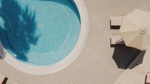 An aerial view of a swimming pool with a circular shape, surrounded by a light-colored deck. - Cavo Notos Beach Hotel (Lefkimmi)