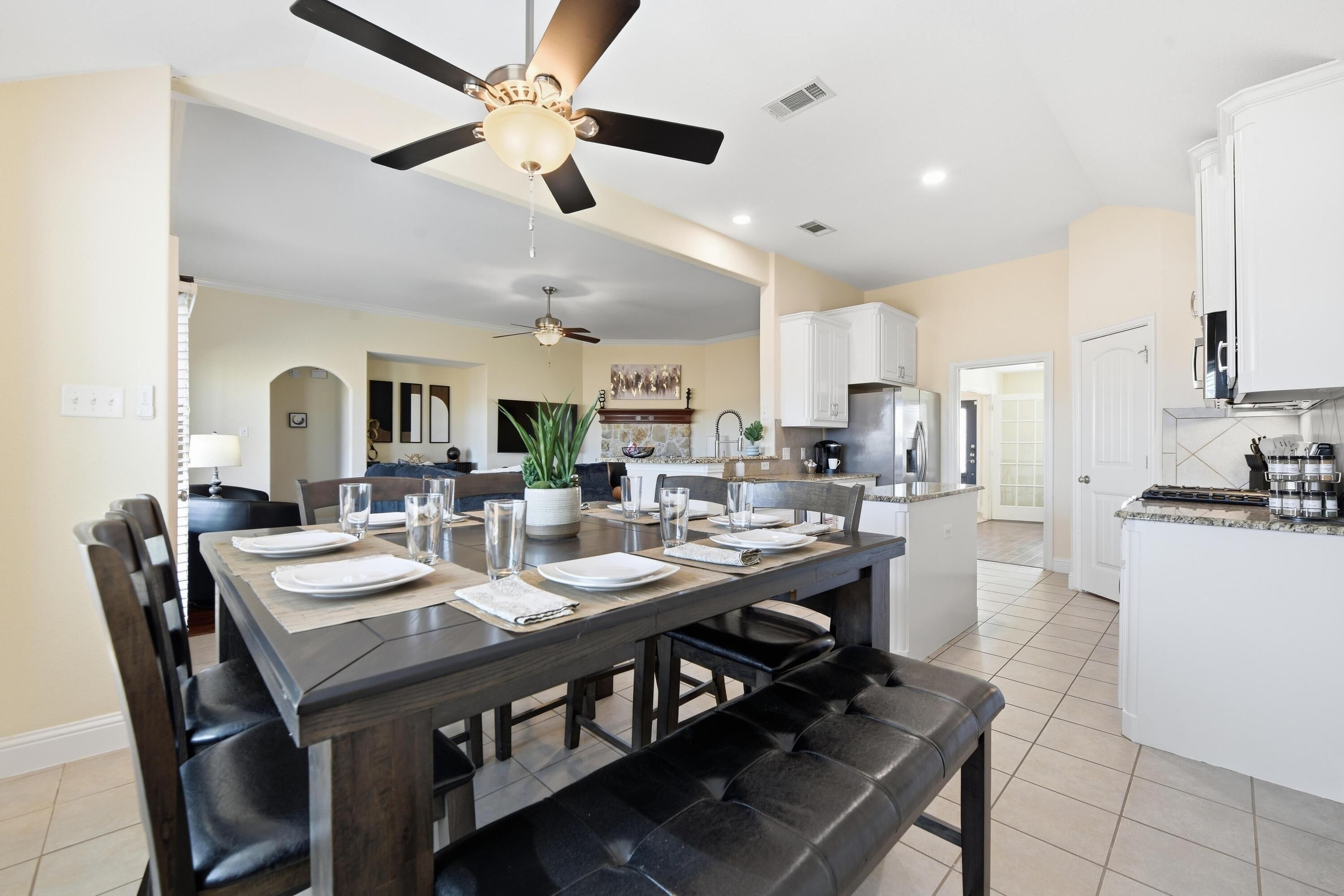 A modern kitchen with white cabinets, a central island, and a dining area with a dark wooden table and chairs.