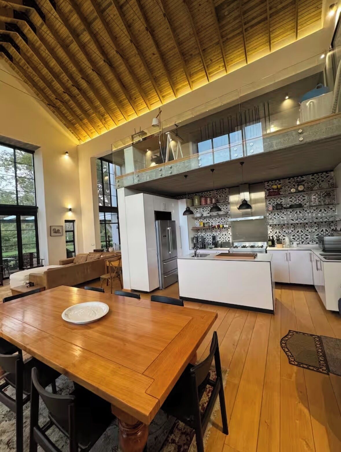 A modern kitchen with a wooden dining table, a built-in island, and a high ceiling with exposed beams.