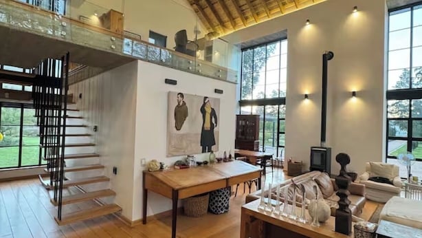 Amplia sala de estar con techo alto, escalera de madera y ventanas grandes.