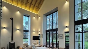 Amplia sala de estar con un sofá grande, una mesa de comedor de madera y una chimenea. Hay ventanas grandes que ofrecen luz natural y vistas al exterior.