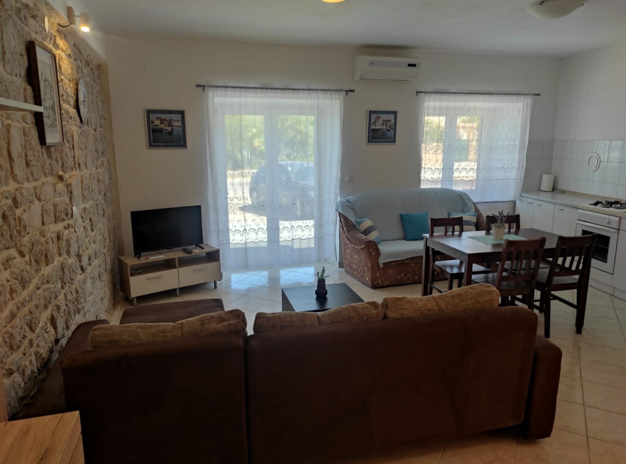 Una sala de estar con pared de piedra, televisor, sofá y comedor con mesa y sillas.