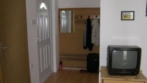 A room with a wooden floor, a television on a wooden cabinet, a door with a white frame, and a coat hanging on the wall. - Apartments Zlatko - Studio apartment with sea view A2 +1 (Prvic Luka)