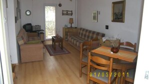 Ein gemütliches Wohnzimmer mit einer Couch, einem Esstisch mit Stühlen, einem Fernseher und einer Uhr an der Wand.