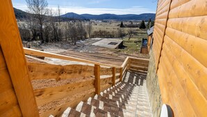 A wooden staircase leading to a balcony with a view of a rural landscape and distant hills. - Villa Vila Velebita - Three Bedroom Countryside Villa (Otocac)
