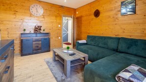A cozy room with wooden walls, a green sofa, a wooden coffee table, a clock, and a desk with drawers. - Villa Vila Velebita - Three Bedroom Countryside Villa (Otocac)