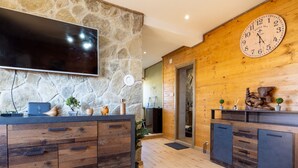 A modern kitchen with a stone wall, wooden cabinets, a large clock, and a flat-screen TV. - Villa Vila Velebita - Three Bedroom Countryside Villa (Otocac)