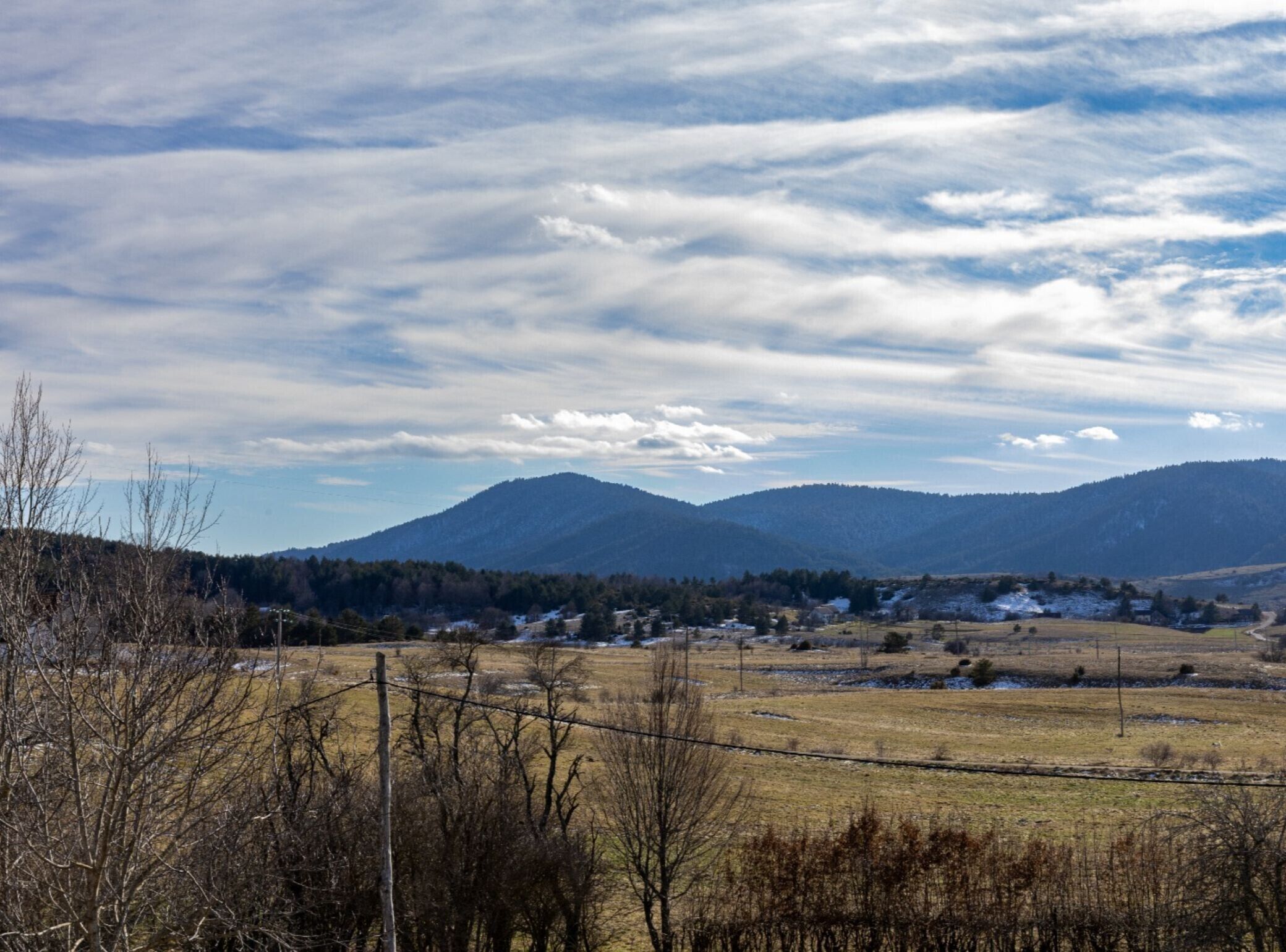 Ländliche Landschaft mit Bergen, blauem Himmel und einigen Häusern im Tal.