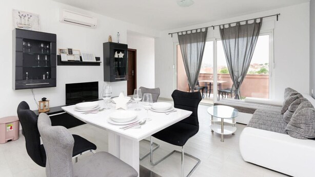 Una sala de estar moderna con una mesa de comedor lista para cuatro personas, un sofá y un televisor.