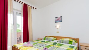 Un letto matrimoniale con una coperta a righe colorate, due cuscini e asciugamani arrotolati. Si nota anche un comodino e un punto luce fissato alla parete.