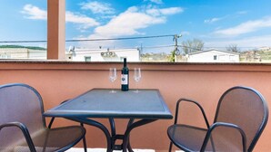 Un balcone con tavolo e sedie, una bottiglia di vino e bicchieri da vino.