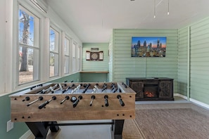 A room with a foosball table, a dartboard, and a fireplace.