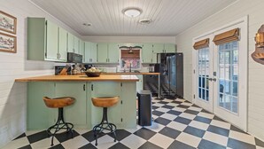 Uma cozinha com piso xadrez, armários verdes e dois bancos de madeira.