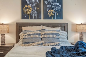 A neatly made bed with patterned pillows, a dark wooden headboard, and two wall-mounted lamps on either side.