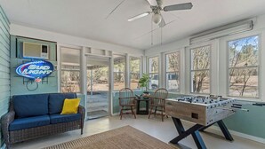 Um quarto com uma mesa de pebolim, um sofá com um travesseiro amarelo e um letreiro da Bud Light.