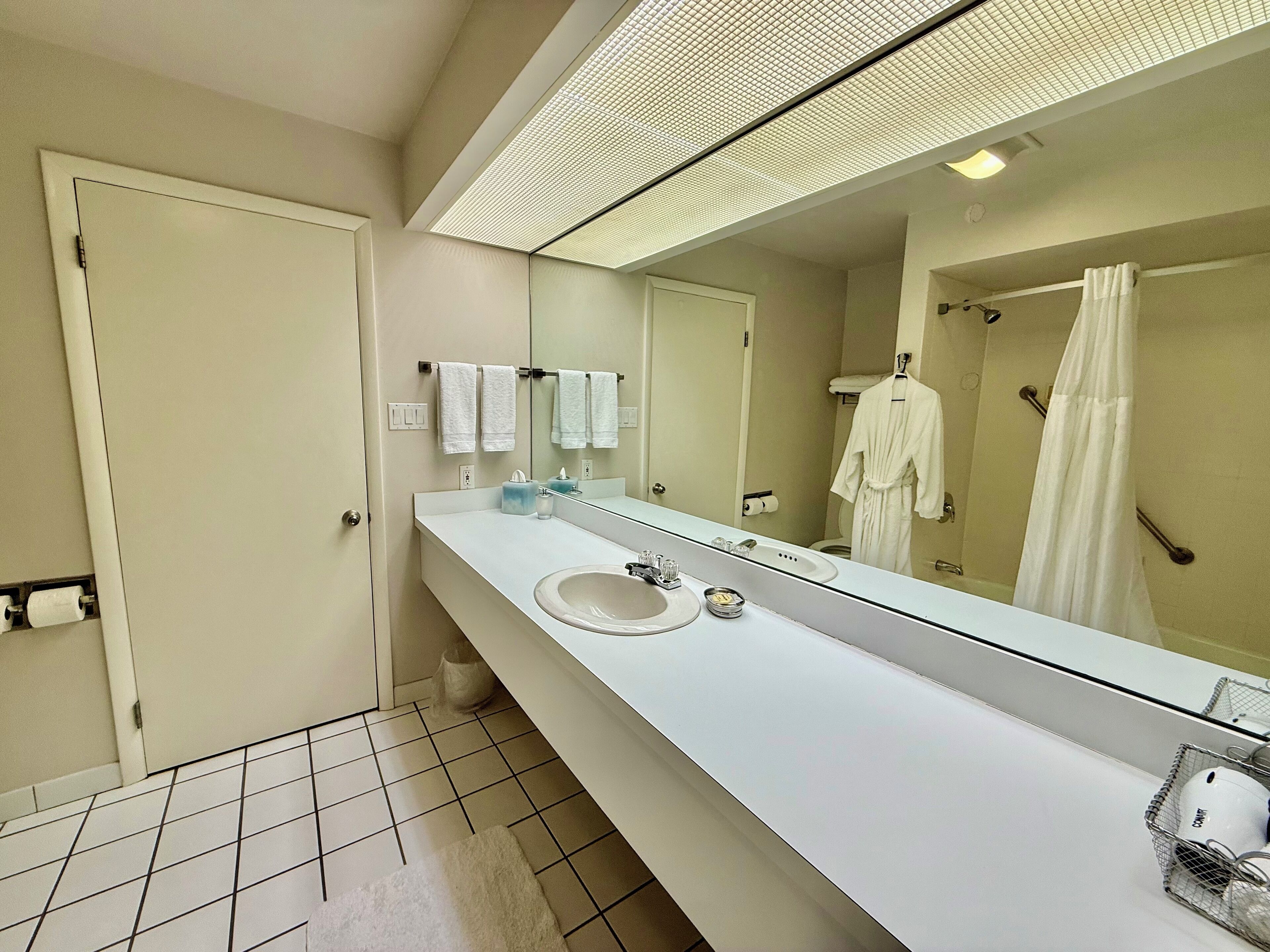 A modern bathroom with a large mirror, white sink, and a shower area.