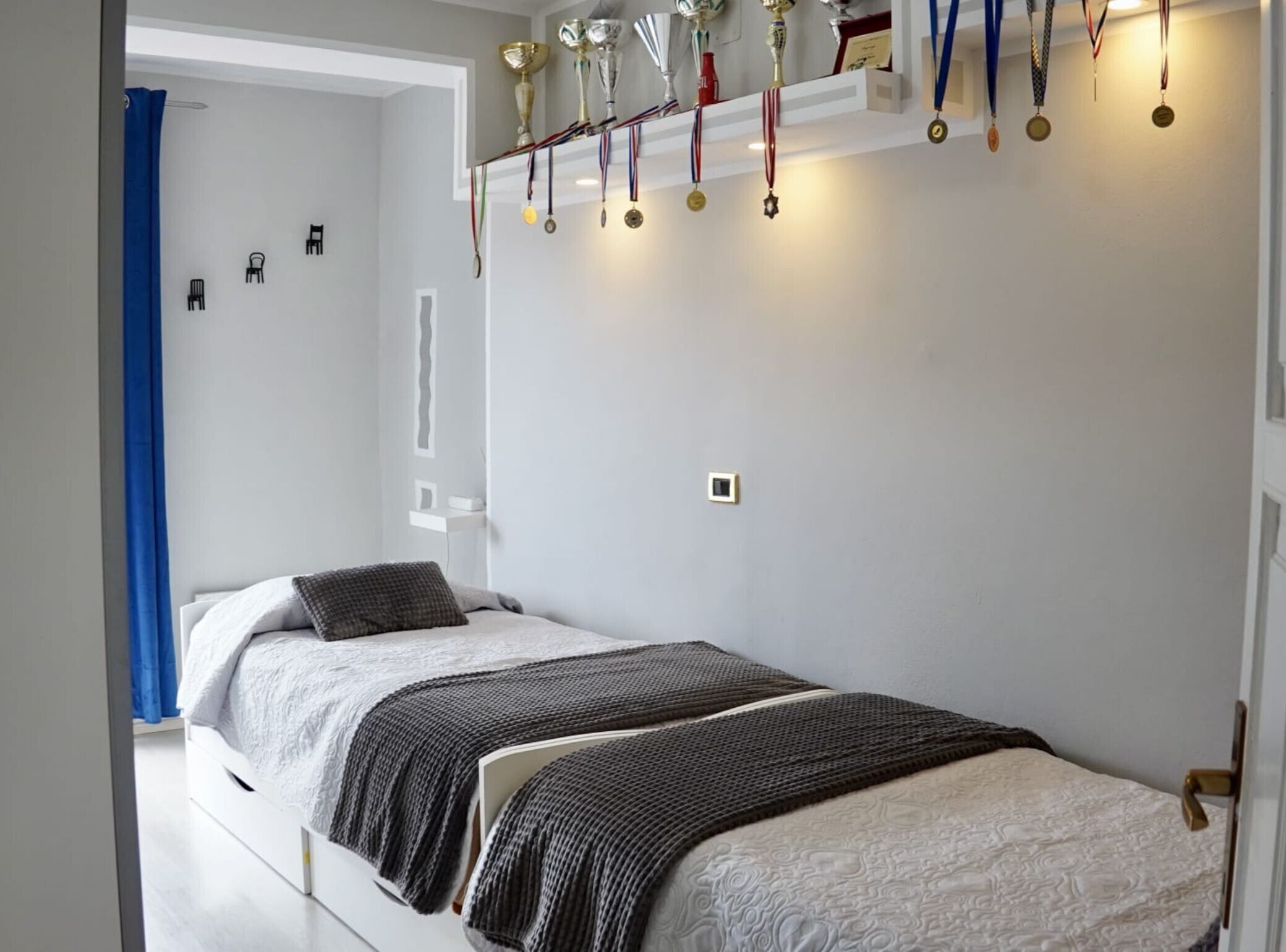 A bedroom with a bed, a blue curtain, and a wall with medals.