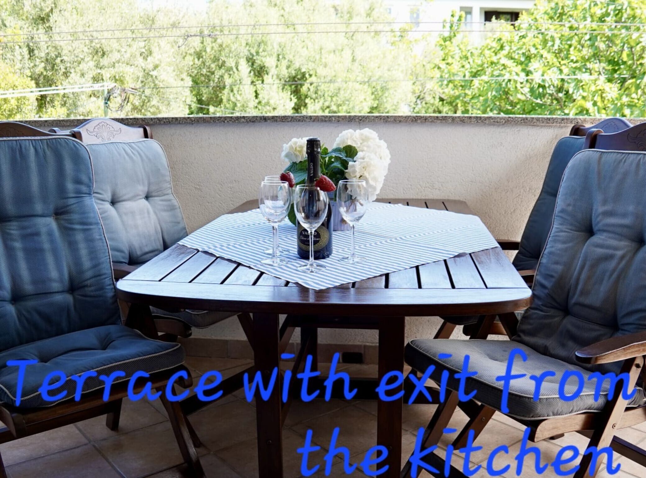 A terrace with a table set for two, featuring a bottle of wine, glasses, and a vase with flowers.