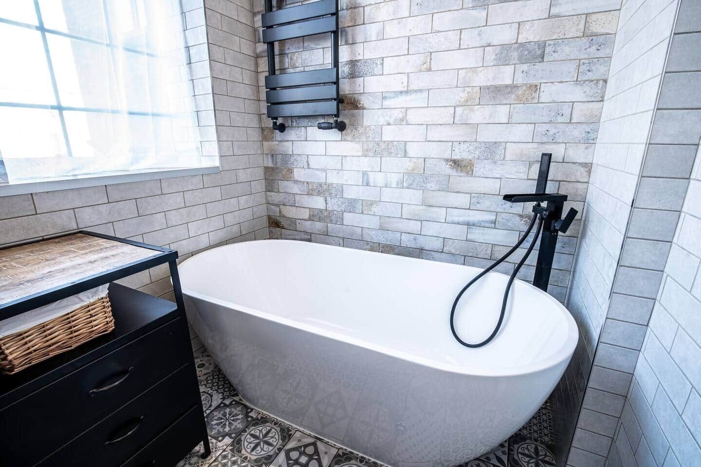 Une salle de bain avec une baignoire sur pieds, une étagère noire et des carreaux de sol à motifs.