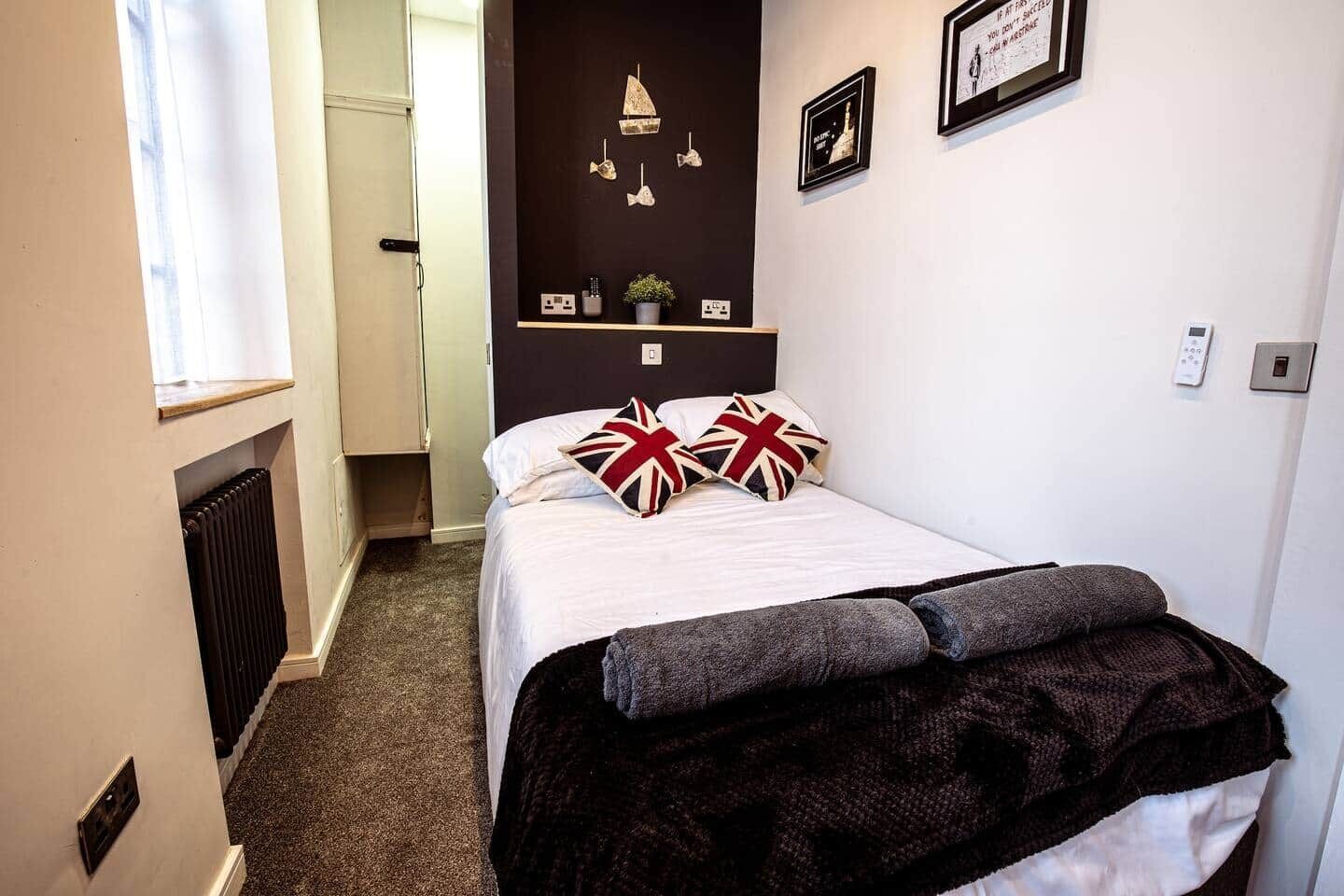 A bedroom with a bed, pillows, a shelf with decorative items, and a radiator.