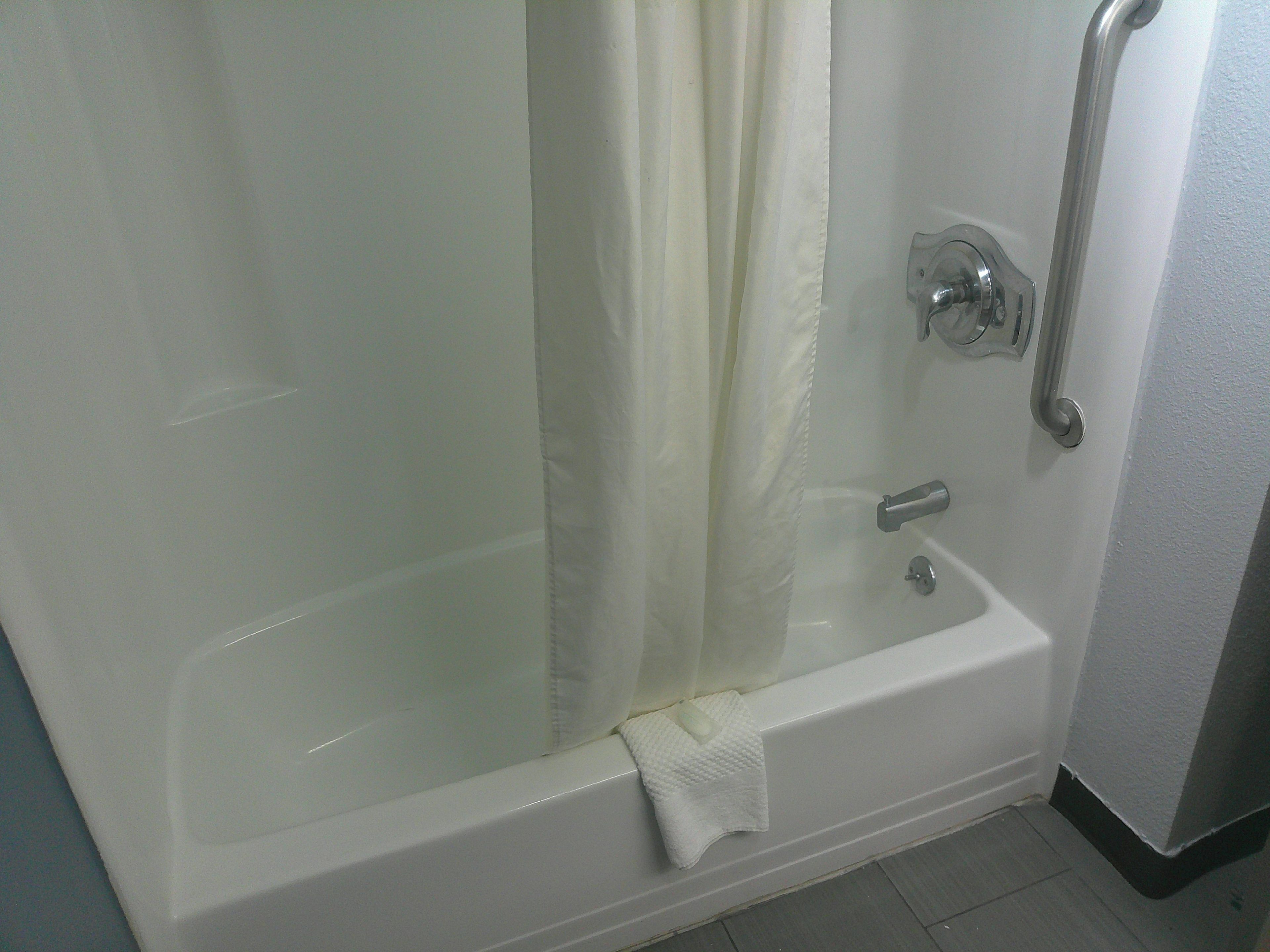 A white bathtub with a shower curtain, a grab bar, and a towel on the floor.