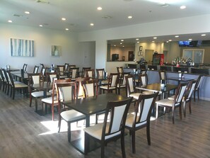 A spacious dining area with multiple tables and chairs, a bar area with a counter, and a television mounted on the wall. - HomeTowne Studios by Red Roof Leesburg (Leesburg)