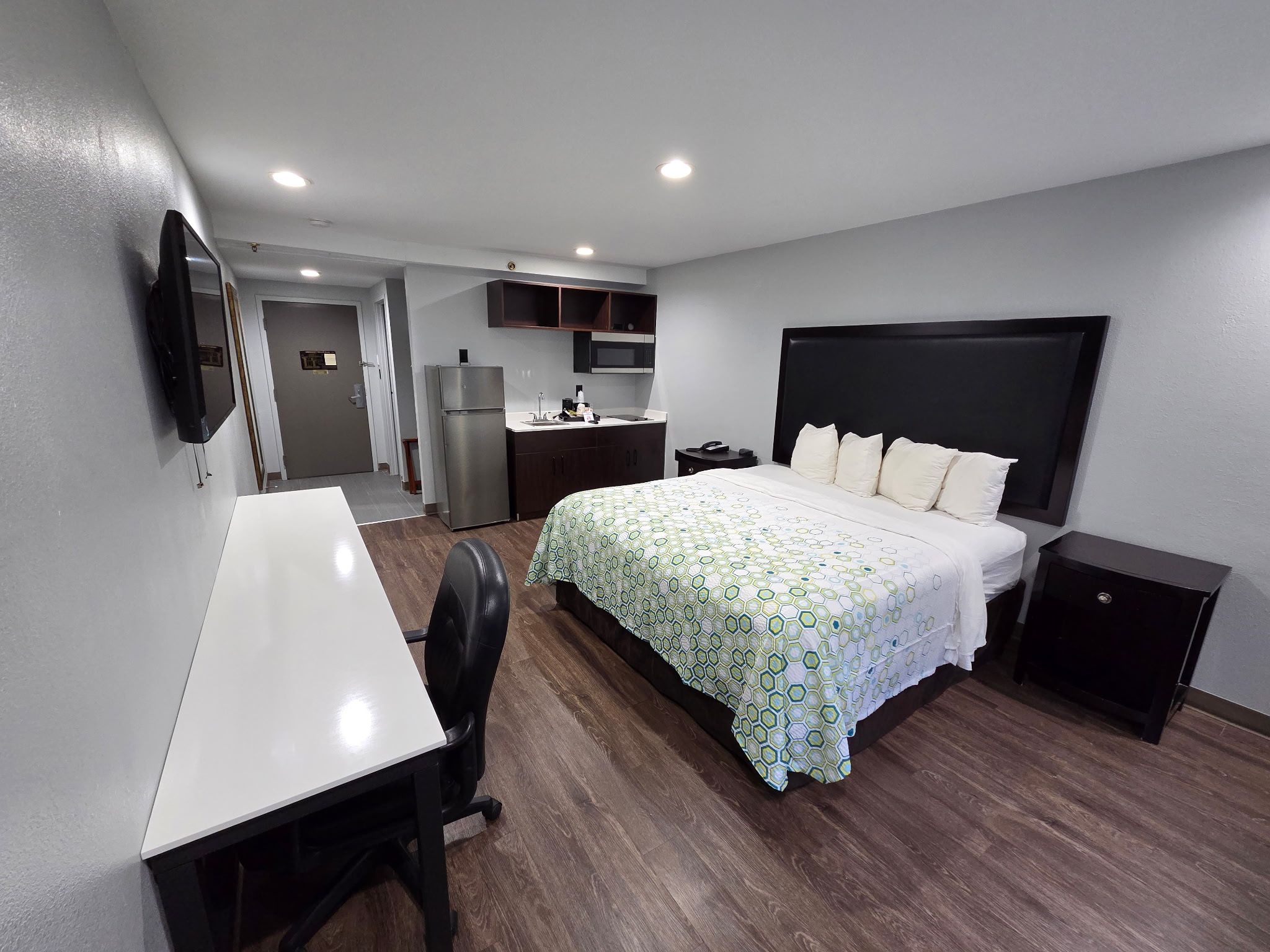 Una habitación de hotel con cama, mesita de noche, escritorio, silla y una zona de kitchenette.