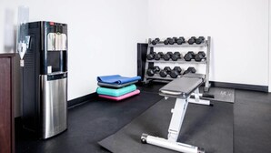 A gym with a water dispenser, dumbbells, a bench, and step platforms.