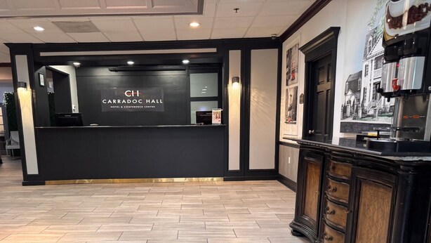 A hotel reception area with a modern design, a reception desk, and a coffee machine. - HomeTowne Studios by Red Roof Leesburg (Leesburg)