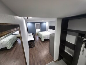 Habitación de hotel compacta con dos camas, un escritorio y una kitchenette pequeña.