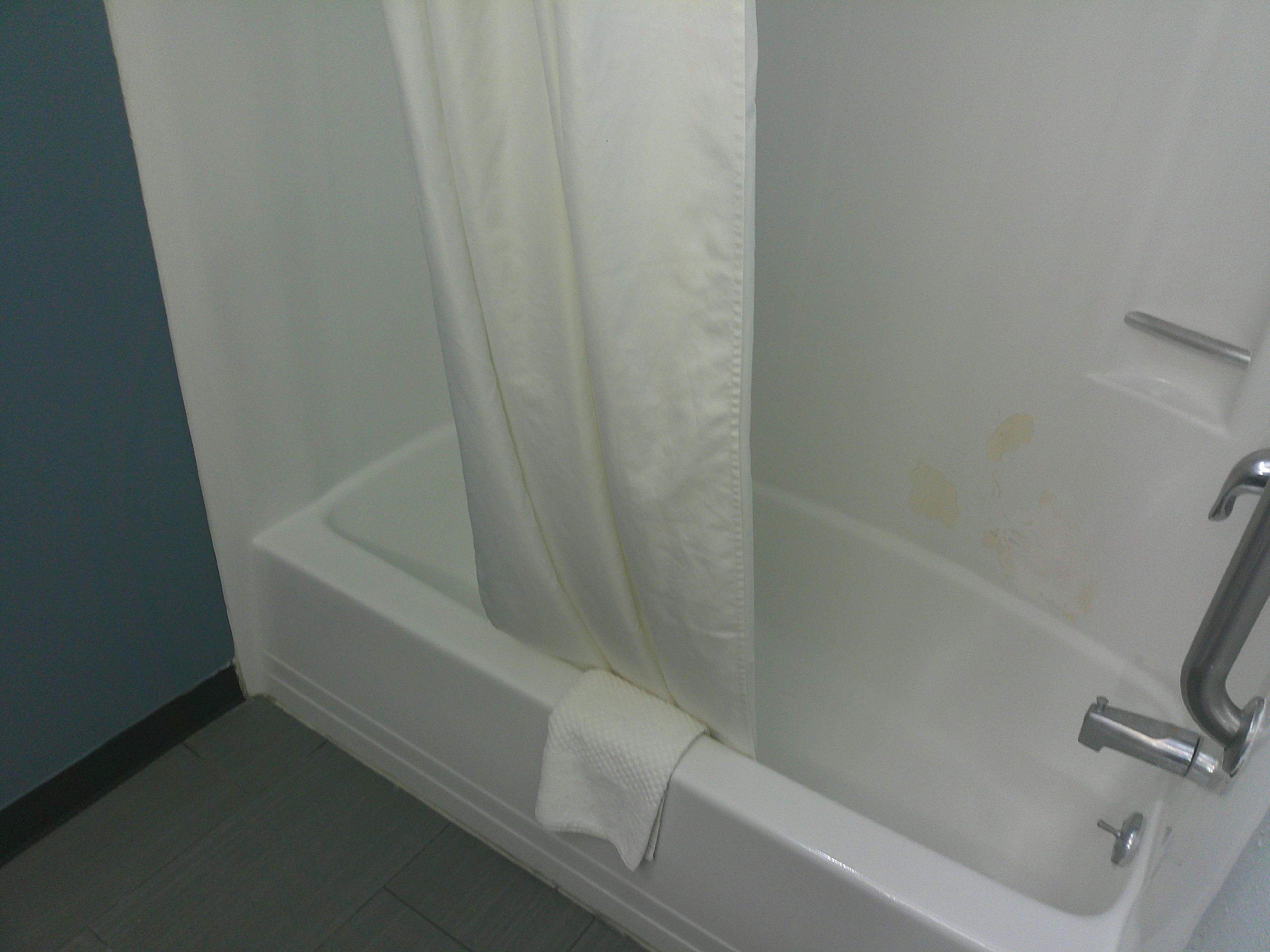 Una bañera blanca con cortina de ducha, una toalla y un grifo.