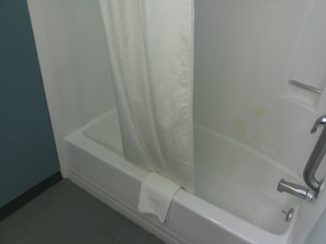 Una bañera blanca con cortina de ducha, una toalla y un grifo.