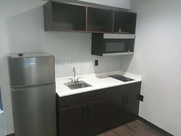 A compact kitchen with a built-in refrigerator, a microwave, a sink, and dark cabinetry. - HomeTowne Studios by Red Roof Leesburg (Leesburg)