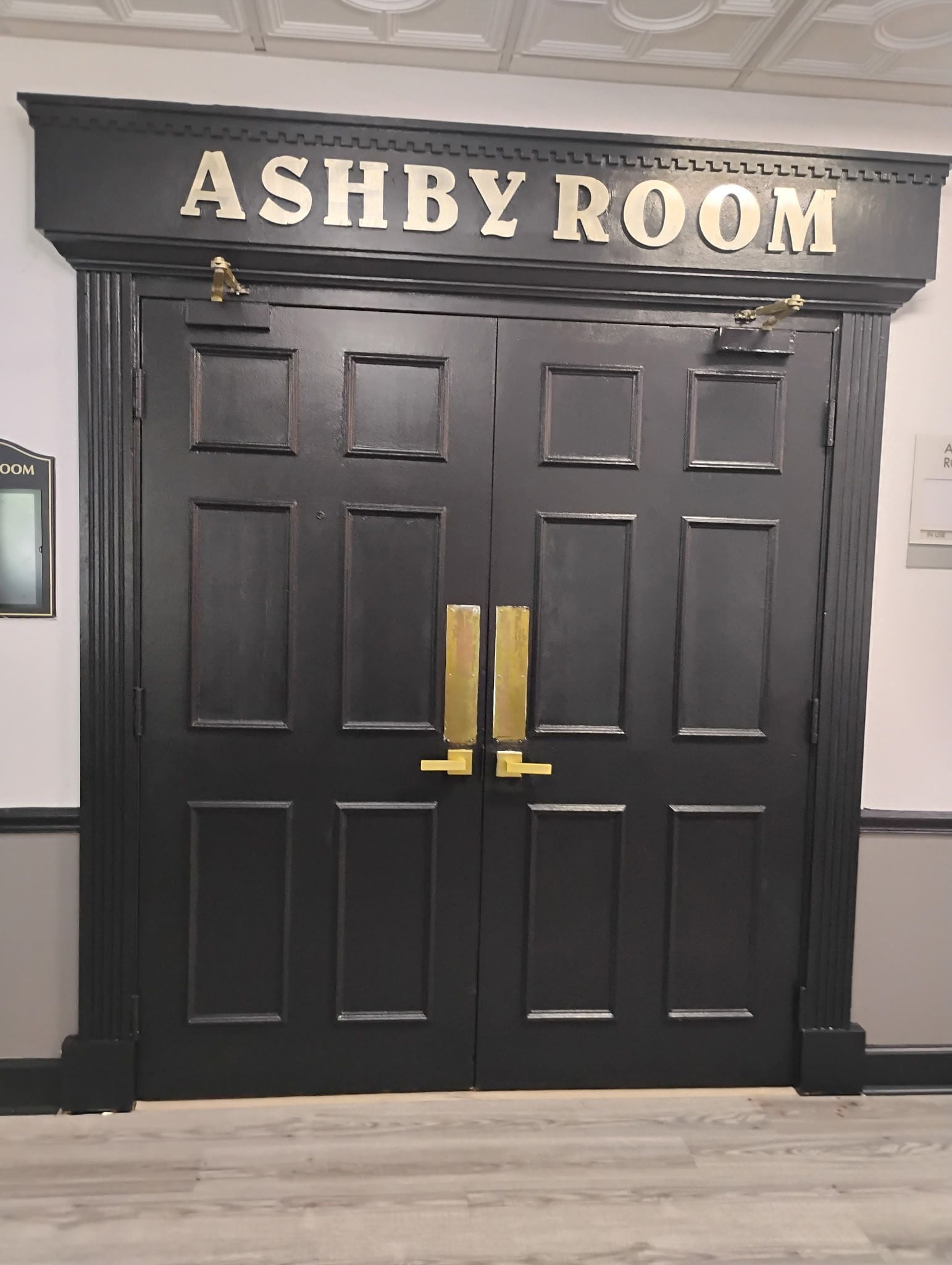 Una puerta doble negra con un letrero que dice 'ASHBY ROOM'.