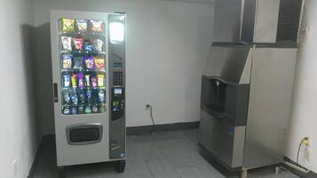 A vending machine and a refrigerator in a room with tiled flooring and a plain wall.