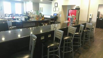A bar area with a long counter, multiple chairs, and a refrigerator.