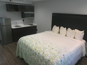 A hotel room with a bed, a small kitchenette, and a dark headboard. - HomeTowne Studios by Red Roof Leesburg (Leesburg)