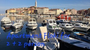 Satamassa on ankkuroituina veneitä, taustalla näkyy kaupunkimaisema, ja tekstissä kerrotaan, että kyseessä on Vila Tena Rovinj, Kroatia, ja että siellä on asunto, johon mahtuu 2+2 henkilöä.