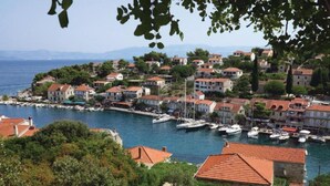 Une ville côtière aux bâtiments aux toits de tuiles rouges, un port de plaisance avec des bateaux, et un paysage montagneux en toile de fond.