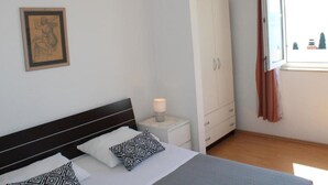 A bedroom with a bed, a nightstand, a wardrobe, and a window with curtains. - Apartments Rubić - Onebedroom Apartment with Loggia and SeaView (2) (Omis)
