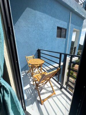 Ein Balkon mit blauer Wand, einem Holztisch und Stühlen sowie Blick auf die Umgebung.