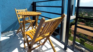 Ein Balkon mit blauer Wand, Holzstühlen, einem Tisch und Blick auf die Umgebung.