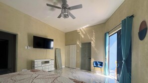 Ein Schlafzimmer mit Bett, Fernseher, Kleiderschrank, einer Tür und einem Deckenventilator.