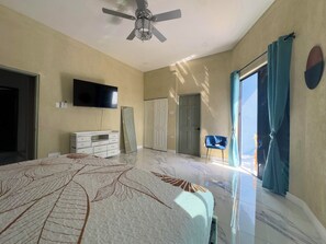Une chambre à coucher avec un lit, une télévision, une armoire, une porte et un ventilateur de plafond.