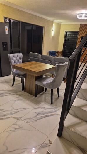 Un espace repas comprenant une table en bois et des chaises rembourrées, un canapé et un escalier.